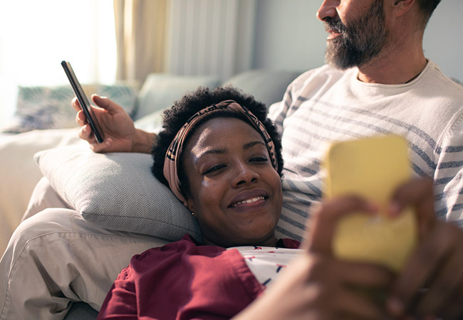 couple relaxing on sofa using smart phones